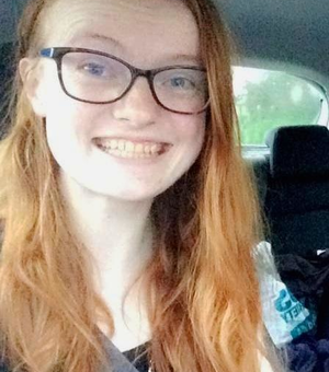 A photo of Lydia smiling at the camera. She has long ginger hair and wears glasses.